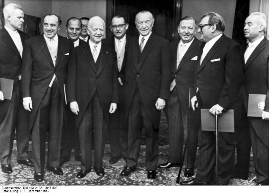 Bundespräsident Lübke hat am 13. Dezember 1962 in seinem Amtssitz den neuen Ministern des Kabinetts Adenauer, die ihm vorher vom Bundeskanzler vorgestellt worden waren, die Ernennungsurkunden überreicht.Ewald Bucher (ganz links) war Mitglied der NSDAP und der SA. Später, von 1962 bis 1965, war er im Kabinett Adenauer V Bundesminister der Justiz. Quelle. Bundesarchiv, Bild 183-A1221-0046-008 auf Wikimedia Commons. Lizenz: CC BY-SA 3.0 de.