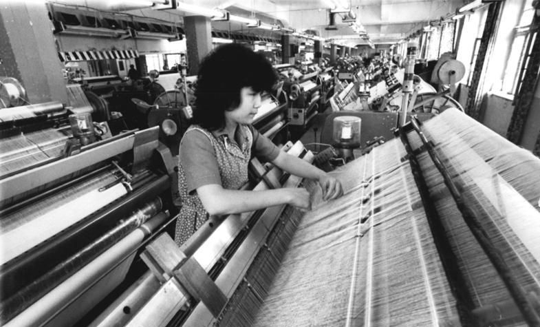 Originale Bildunterschrift des Bundesarchivs: ADN-ZB Thieme 16.7.85 Bez. Karl Marx-Stadt: Wettbewerb, Eine Ausbildung als Weberin erhält Nguyen Thi aus der SR Vietnam gemeinsam mit weiteren fünf Mädchen gegenwärtig im VEB Vowetex Plauen. Für ihre Qualitätsarbeit wurde sie bereits mehrmals als beste Weberin der Jugendbrigade "Artur Becker" ausgezeichnet. Im Werk Treuen dieses Betriebes werden Schichtträgergrundgewebe für die Kunstlederindustrie und Bucheinbandgewebe für grafische Großbetriebe produziert. Im ersten Halbjahr konnten die Werktätigen zwei Tage Planplus abrechnen., Quelle: Wikimedia Commons, Lizenz: Bundesarchiv, Bild 183-1985-0716-003 / CC-BY-SA 3.0.