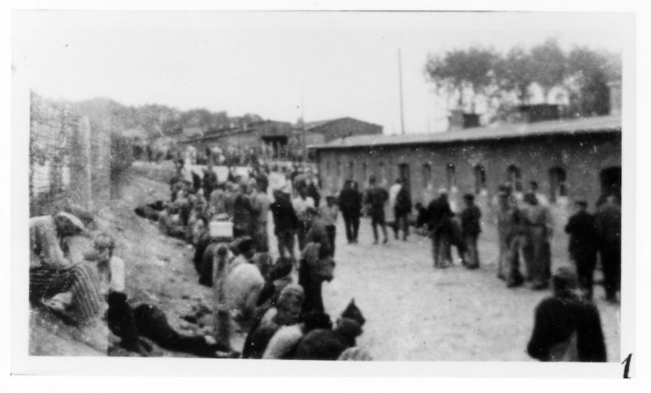Häftlinge sitzen an und laufen über eine Gasse vor dem Latrinen- und Waschraumgebäude im »Kleinen Lager«, Juni 1944. Foto: Georges Angéli. Quelle und Lizenz: Fotoarchiv Gedenkstätte Buchenwald, Signatur 007-01.006