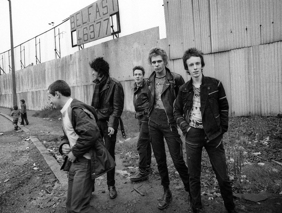 Mick Jones, Joe Strummer, Paul Simonon und Nicky „Topper“ Headon vor einer sogenannten Peace Line in Belfast, Oktober 1977, Quelle: Mit freundlicher Genehmigung des Fotografen Adrian Boot.