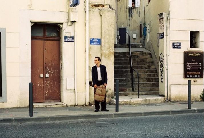 Filmstill aus Transit zeigt Franz Rogowski als Georg verloren vor einer beigen Wand stehend