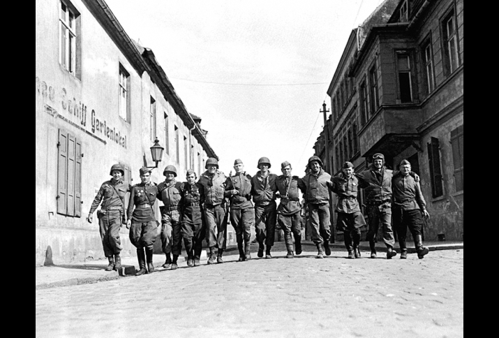 Amerikanische und sowjetische Soldaten laufen Arm in Arm in einer Reihe auf einer Straße im deutschen Torgau
