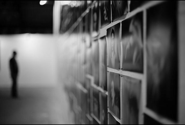 Schwarzweißfoto: Unscharfe Aufnahme eine(r) Ausstellungsbesucher*in vor einer Fotowand