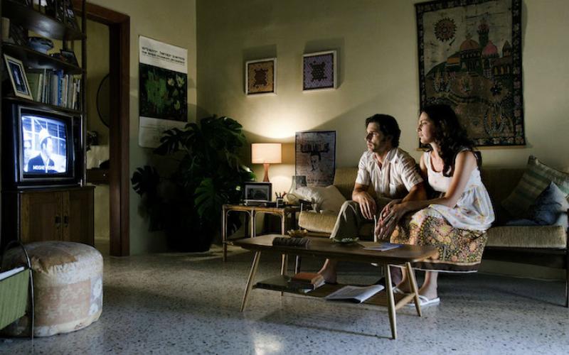 Avner Kaufman (Eric Bana) und Daphna Kaufman (Ayelet Zurer) sitzen vor dem Fernsehen