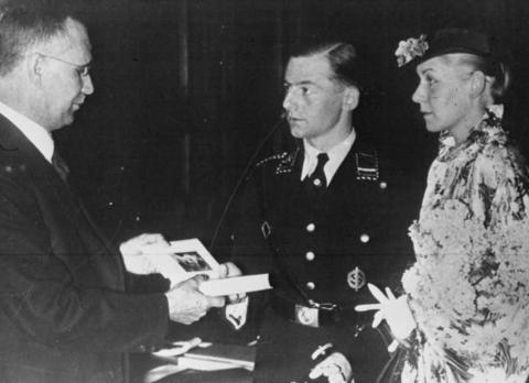 A wedding ceremony in Germany in 1936. Translation of caption: "Chancellor Hitler has decided that a copy of his book Mein Kampf will be given to every couple on their wedding day.", 1936, Bibliothèque nationale de France, Wikimedia Commons, Public Domain. 