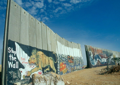 Die noch unfertige Begrenzungsmauer, die Teile von Bethlehem abtrennt um Israel vor palästinensischen Terroristen zu schützen. Die Zeichnungen scheinen von pro-palästinensischer Seite zu stammen, die dünne rote Beschriftung von pro-isralischer Seite. Eini