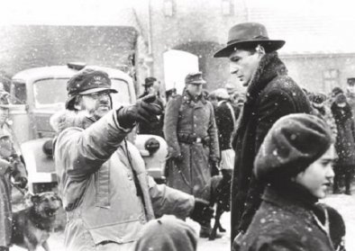 Film Still aus Schindlers Liste das Oskar Schindler in seiner Fabrik zu den jüdischen Arbeiter*innen sprechend zeigt