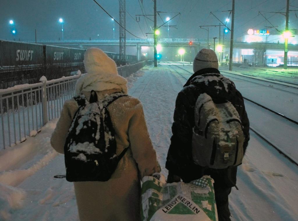 Ein Paar geht in einer verschneiten Winterlandschaft an Eisenbahngleisen entlang