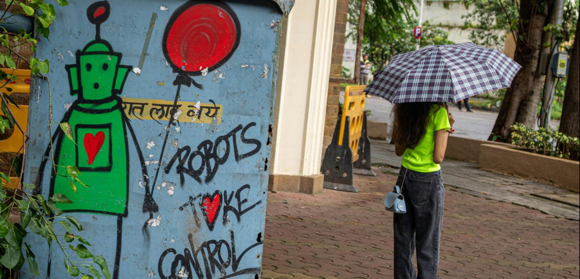 Links ein Graffiti mit der Aufschrift "Robots take control", rechts eine junge Frau mit Regenschirm