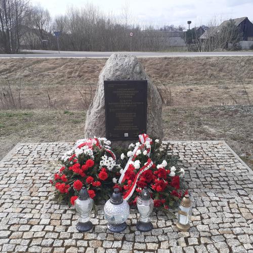 Denkmal an dem Ort der ehemaligen Bahnhofsstation im Dorf Treblinka, 31. März 2026. Die Kränze wurden vom Pilecki Institut (Witold Pilecki Institute of Solidarity and Courage) und vom Bürgermeister und den Bewohnern der Gemeinde Małkinia gestiftet; rechts eine goldene Kerze mit der goldenen Inschrift „Treblinka Museum – wir erinnern” 
