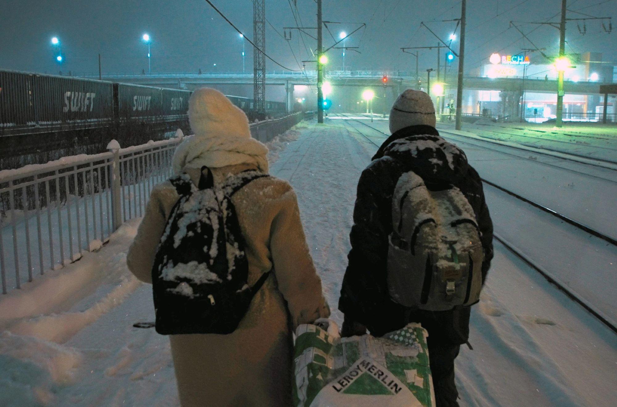 Ein Paar geht in einer verschneiten Winterlandschaft an Eisenbahngleisen entlang