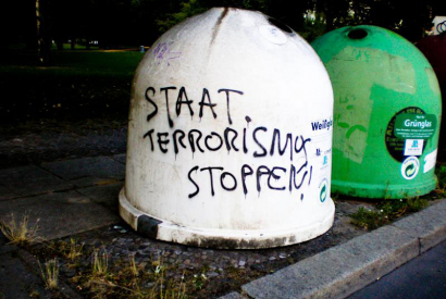 Glaßmülltonne mit der Aufschrift "Staat Terrorismus Stoppen"