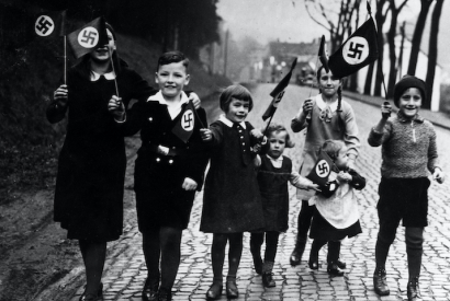 Kinder gehen mit Hakenkreuzfahnen in der Hand spazieren. Propagandafoto für die Presse