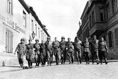 Amerikanische und sowjetische Soldaten laufen Arm in Arm in einer Reihe auf einer Straße im deutschen Torgau