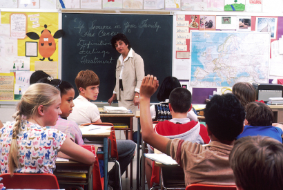 Lehrerin an der Tafel in vollem Klassenzimmer, 1985.